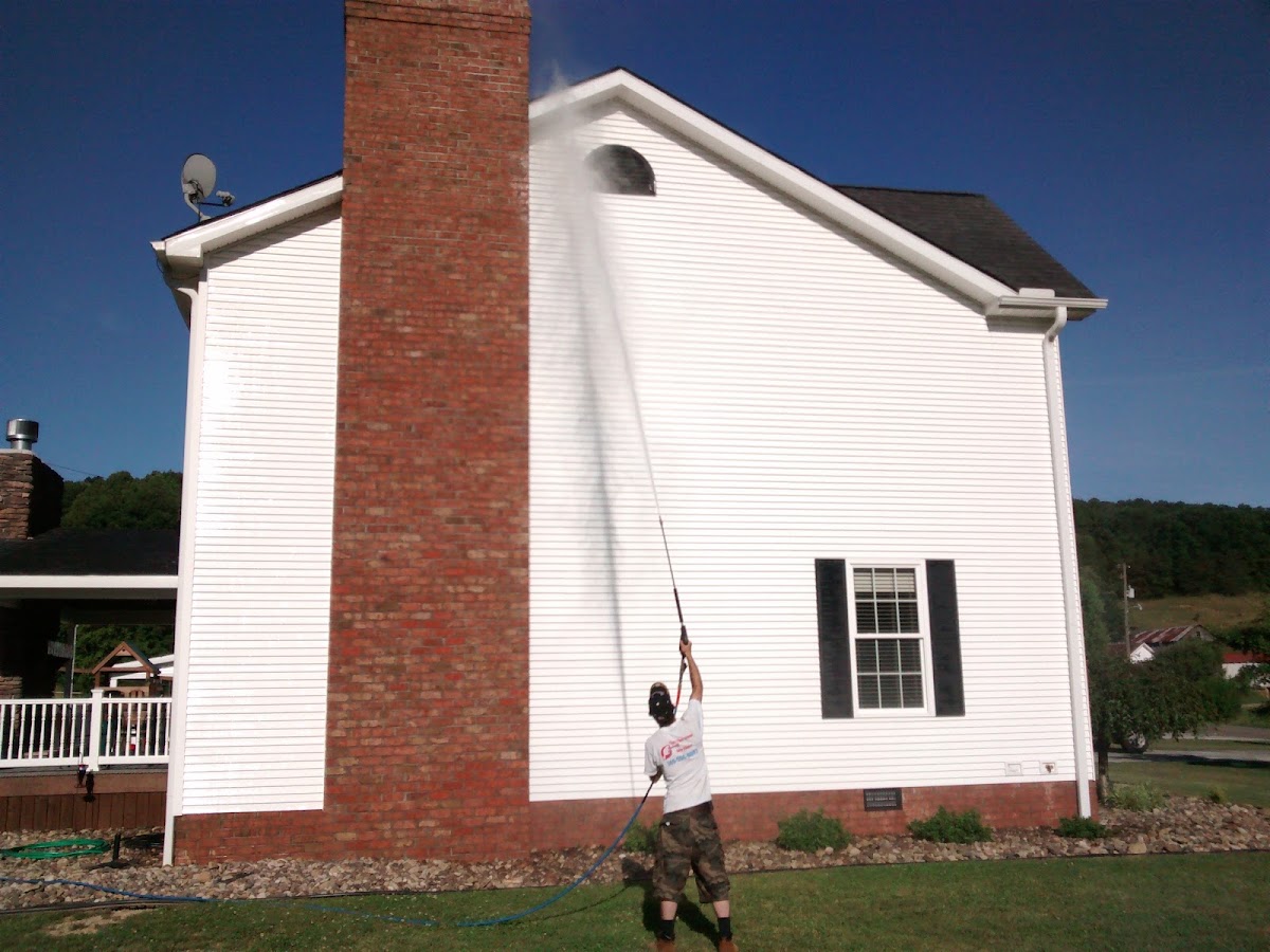 McGinnis crew member washing tall white siding beside a brick chimney